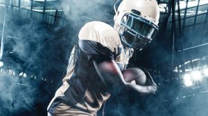Football player holding a football with stadium lights in the background Football player holding a football with stadium lights in the background